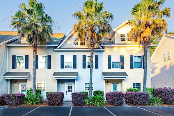 A multi-story building with a symmetrical facade, featuring a central entrance with a door and windows on each floor. - Charming 3-bedroom townhome Near Historic Downtown + Balcony + Lake Access (North Charleston)