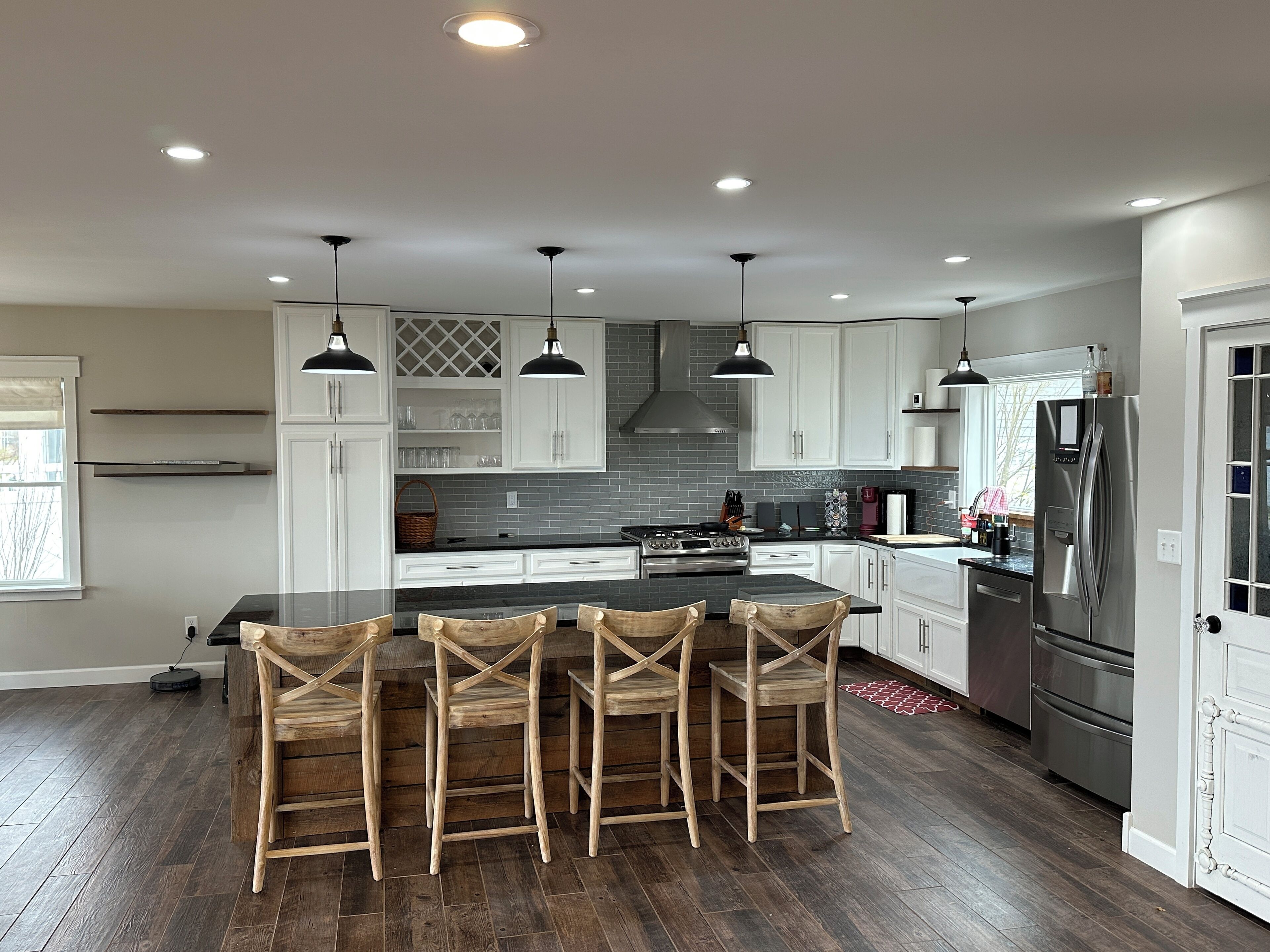 A modern kitchen with a central island, bar stools, white cabinets, and stainless steel appliances.