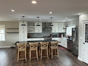 A modern kitchen with a central island, bar stools, white cabinets, and stainless steel appliances. - Beautiful 4-Bedroom Lakefront Home: dock & hot tub, on White Lake, Whitehall, MI (Whitehall)