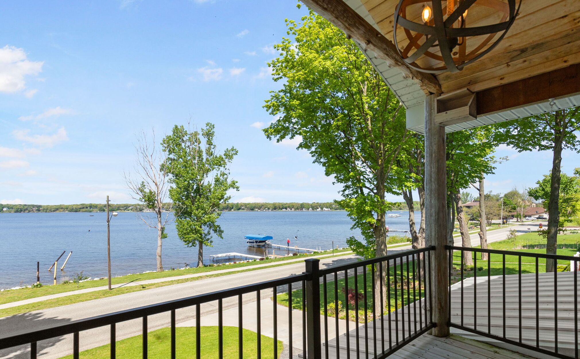 A covered deck with a view of a lake, a dock with boats, and a clear sky.