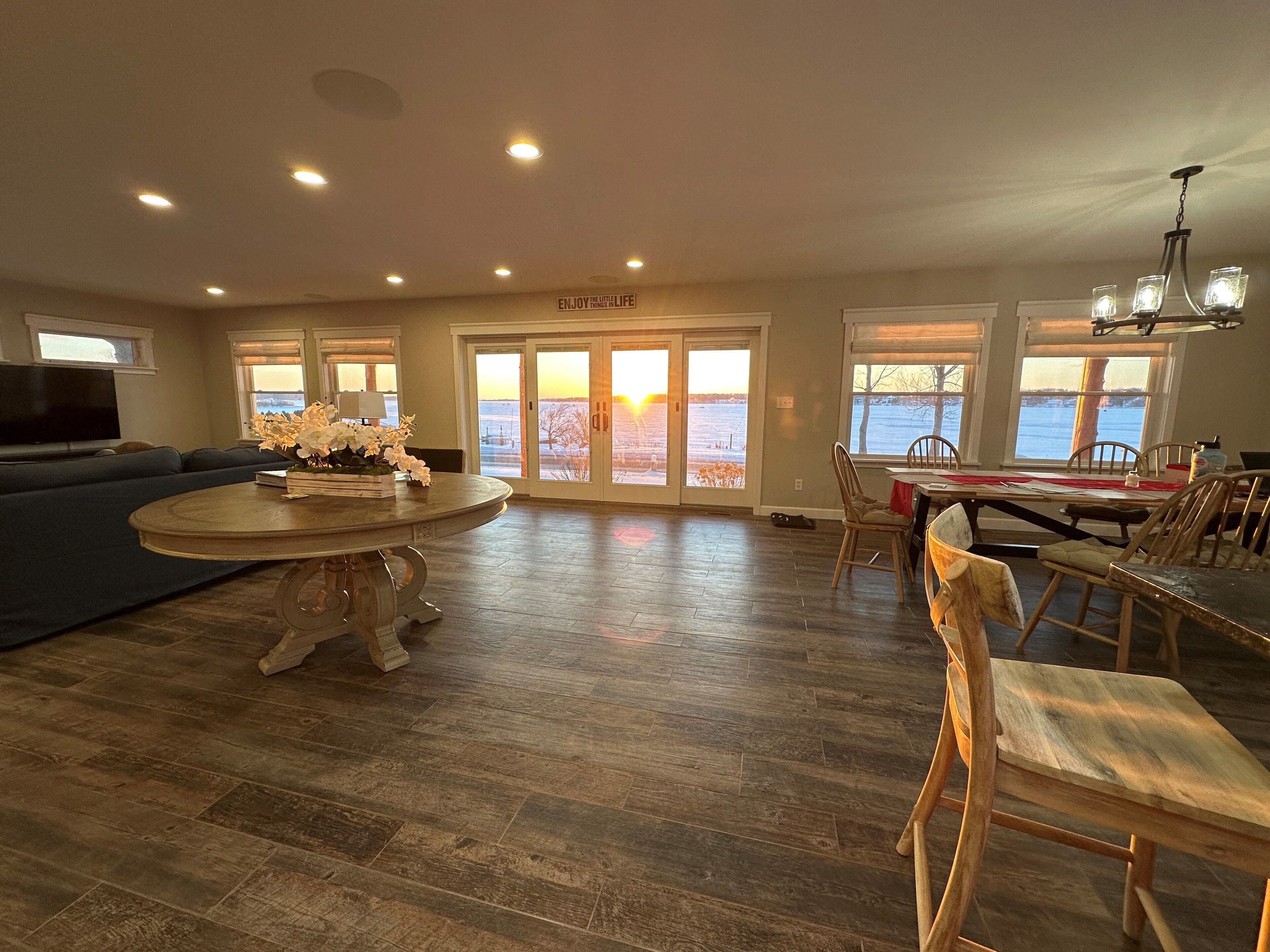 A spacious living room with a large sofa, a dining area with a table and chairs, and a view of a snowy landscape through the glass doors.