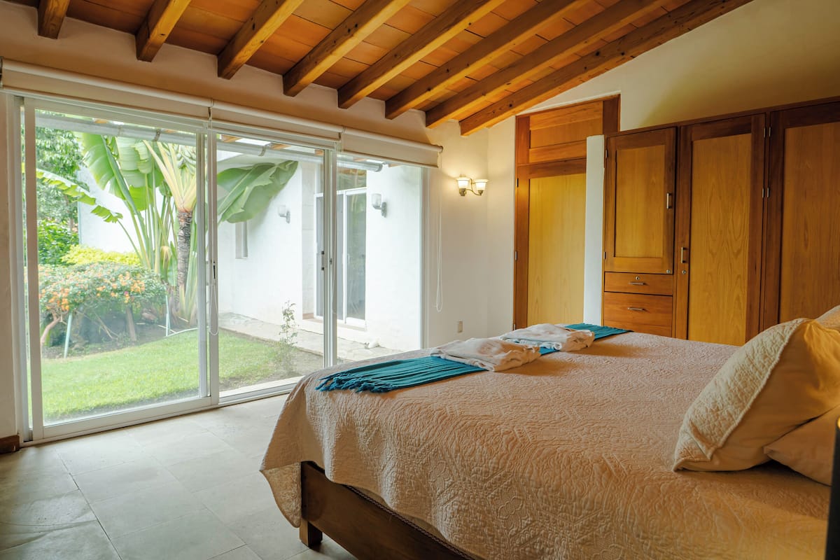 A bedroom with a bed, a sliding glass door to a garden, and wooden cabinets.