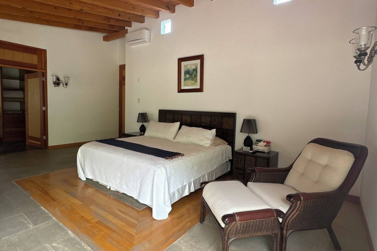A bedroom with a bed, a chair, a nightstand, and a picture on the wall.