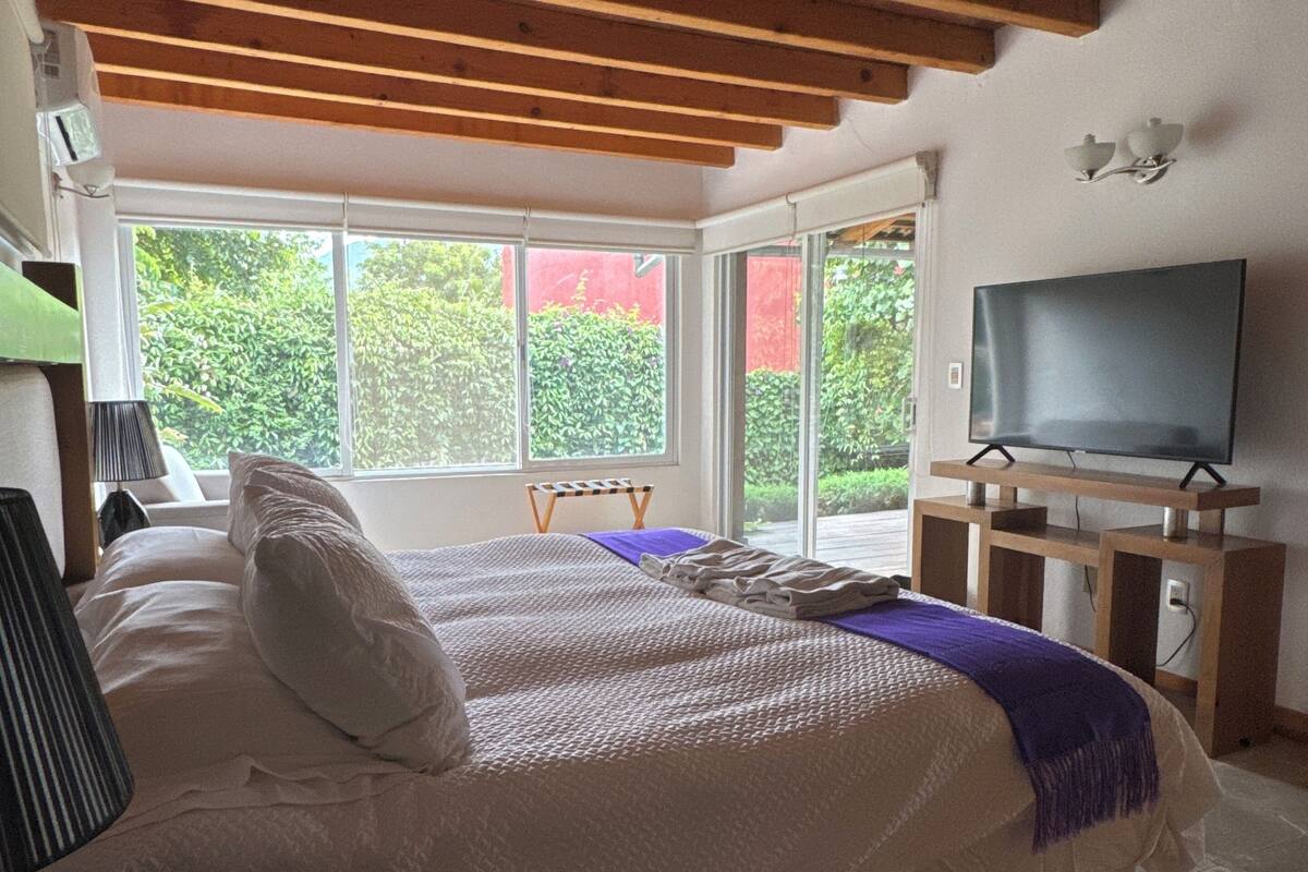 A bedroom with a bed, a TV, and a window with a view of greenery.