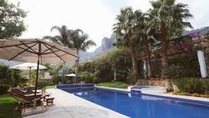 A swimming pool with lounge chairs and umbrellas, surrounded by lush greenery and palm trees. - Finca Catalina Hotel Boutique  (Tepoztlán)