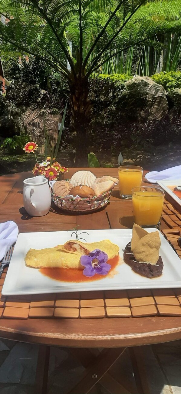 A breakfast setting with a plate of food, a pitcher, and a glass of orange juice on a wooden table outdoors.