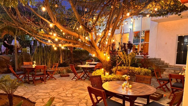 An outdoor patio area with stone flooring, wooden tables and chairs, and string lights. - Finca Catalina Hotel Boutique  (Tepoztlán)