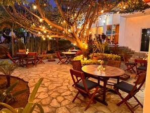 An outdoor patio area with stone flooring, wooden tables and chairs, and string lights.