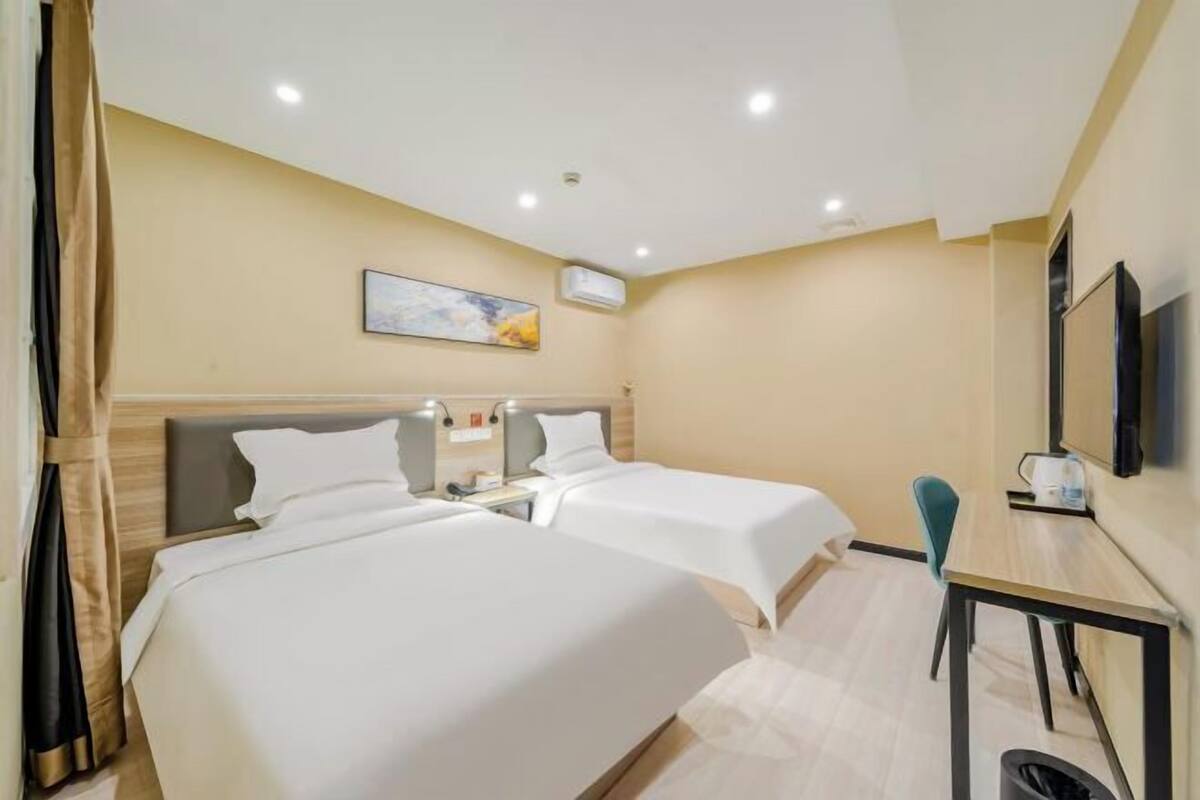 A hotel room with two beds, a desk, a chair, a television, and a painting on the wall.