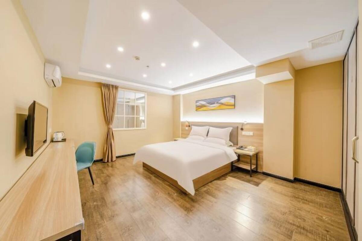 A hotel room with a bed, bedside table, TV, and a desk with a chair.