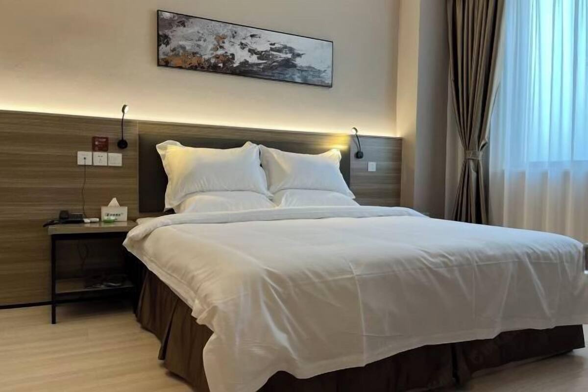 A hotel room with a bed, bedside table, lamp, and a painting on the wall.