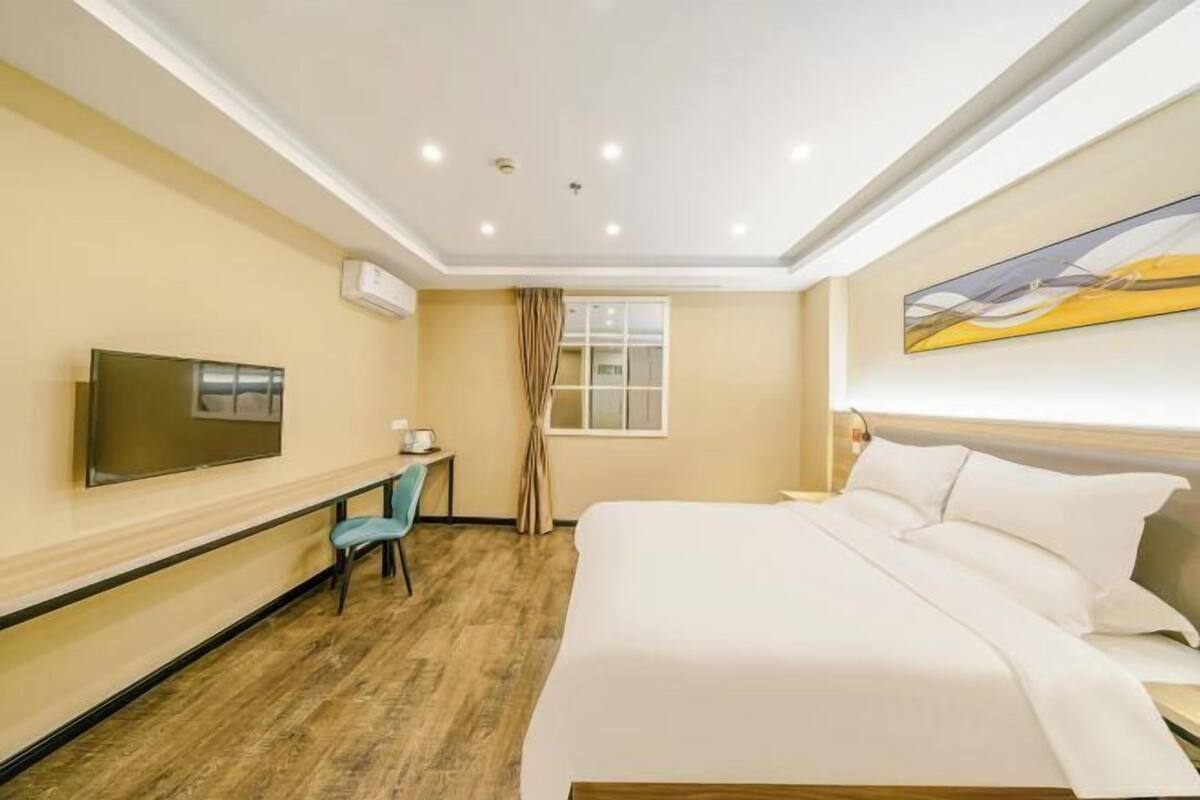 A hotel room with a bed, a desk, a chair, a television, and a window with curtains.