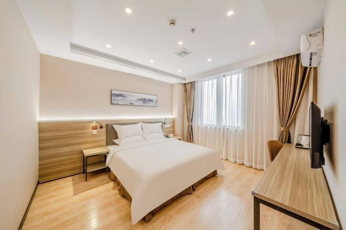 A hotel room with a bed, bedside table, and a desk with a chair.