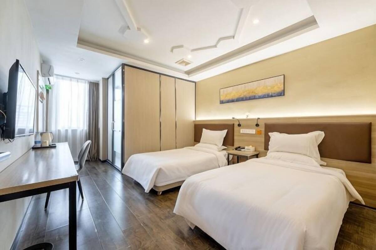A hotel room with two beds, a desk, a TV, and a painting on the wall.
