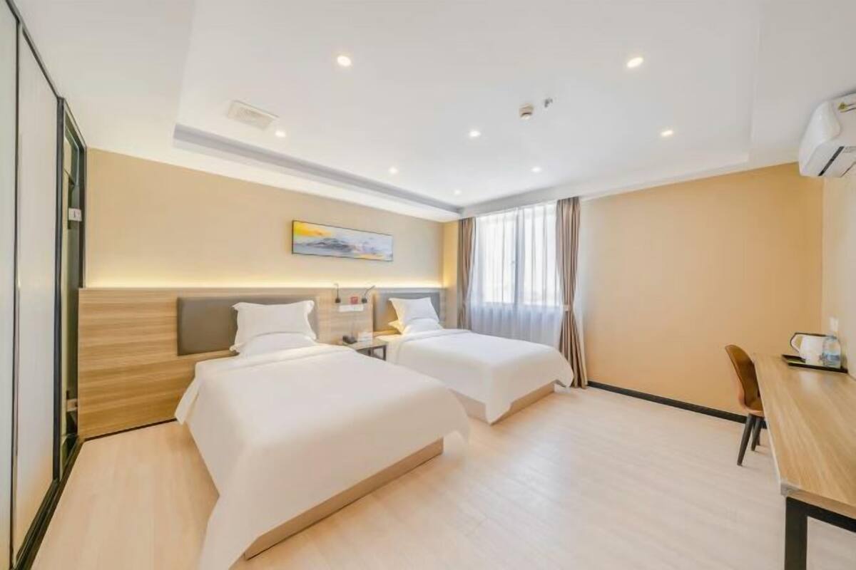 A hotel room with two beds, a desk, a chair, and a window with curtains.