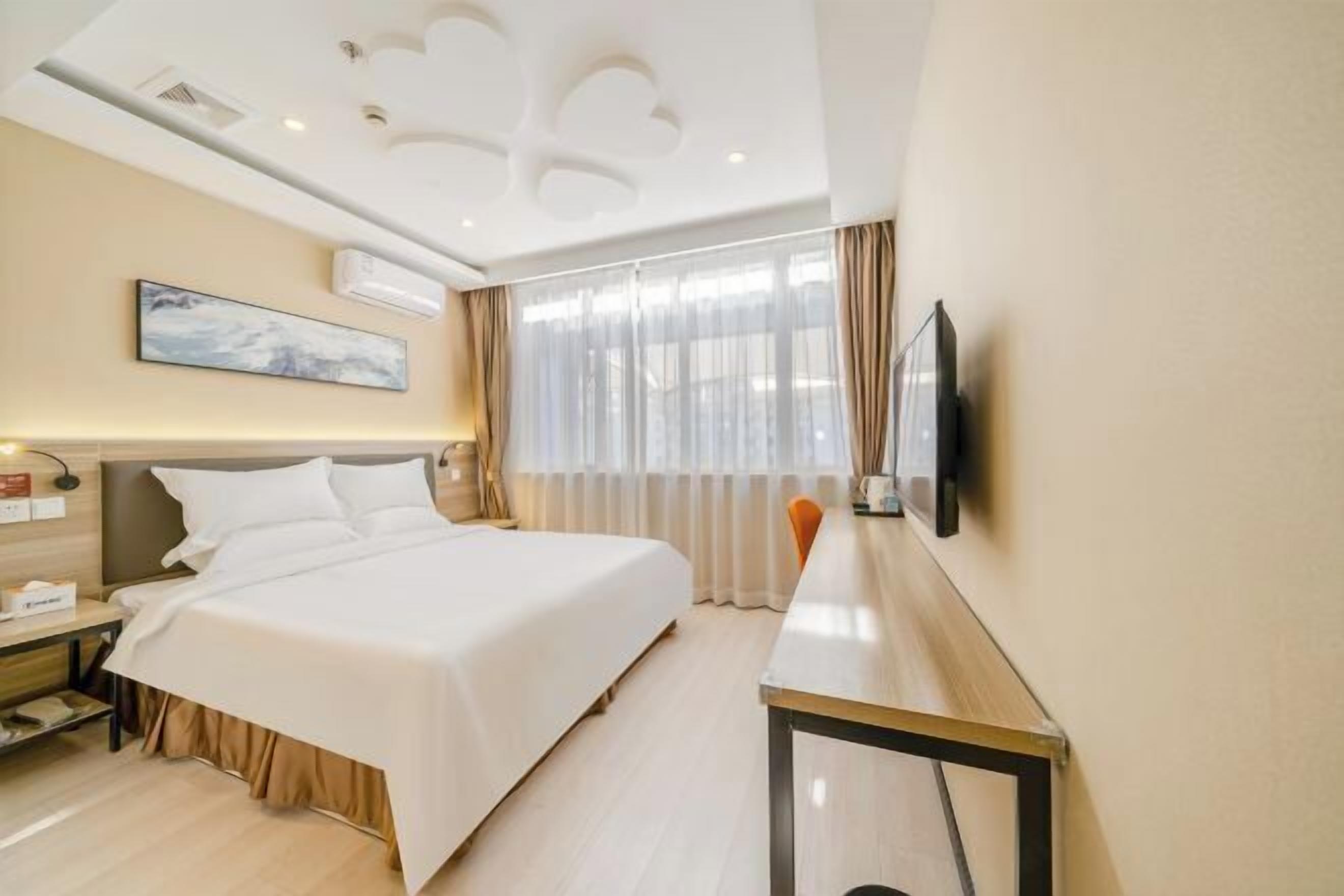 A hotel room with a bed, bedside table, lamp, TV, and a large window with curtains.