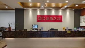 A hotel reception area with a marble counter, a red sign above indicating the hotel name, a television, and a few informational cards. - Songyi Hotel Songjiang University Town Rongfeng Life Square Branch (Shanghai)