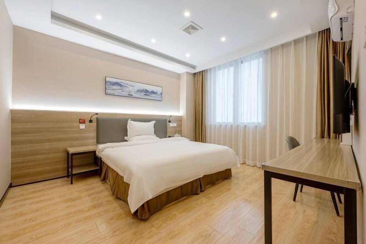 A hotel room with a bed, bedside table, lamp, and a TV.