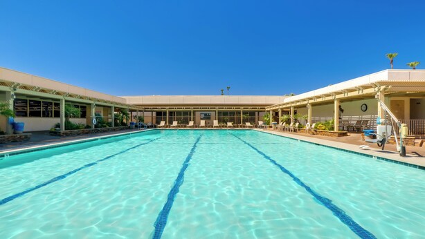 A large indoor swimming pool with clear blue water, surrounded by lounge chairs and a covered seating area. - Swim & Golf: Palm Desert Home in Senior Community! (Palm Desert)