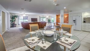 A modern living room with a glass dining table set for six, a brown leather sofa, and a ceiling fan. - Swim & Golf: Palm Desert Home in Senior Community! (Palm Desert)