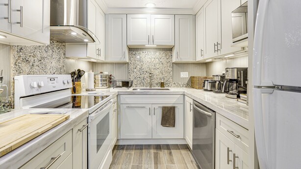 A modern kitchen with white cabinets, a granite backsplash, stainless steel appliances, and a central island. - Oceanside Condo w/ Pool & Hot Tub Access! (Oceanside)