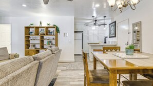 A modern living room with a sofa, wooden bookshelf, dining table, and ceiling fans. - Oceanside Condo w/ Pool & Hot Tub Access! (Oceanside)