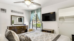 A bedroom with a bed, a dresser, a mirror, a ceiling fan, a TV, and a window with curtains. - Oceanside Condo w/ Pool & Hot Tub Access! (Oceanside)