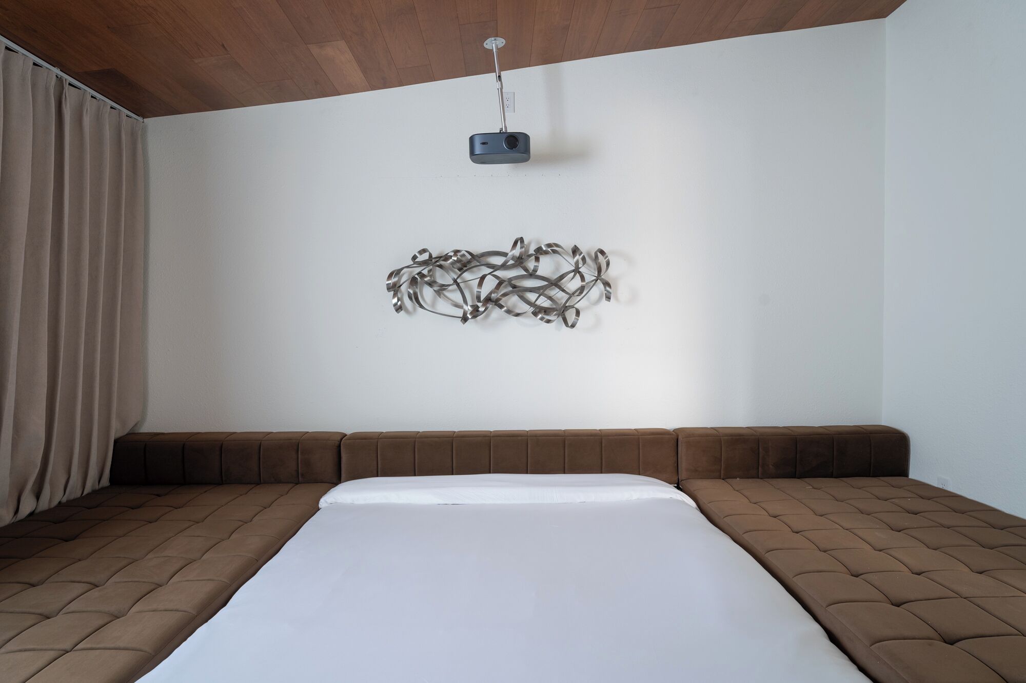 A bedroom with a large bed, a wall-mounted projector, and a decorative metal sculpture.