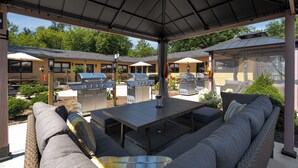 Un patio exterior techado con mesa de comedor, asientos acolchados y parrillas de barbacoa.