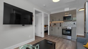 Una cocina moderna con electrodomésticos de acero inoxidable, un televisor de pantalla plana y un comedor con una mesa de madera oscura.