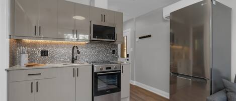 A modern kitchen with stainless steel appliances, grey cabinetry, and a tiled backsplash.