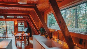 Une cuisine avec des poutres en bois, un long plan de travail et une fenêtre donnant sur une forêt.