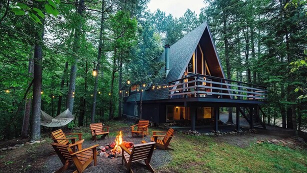 Une cabane dotée d’un foyer extérieur et de sièges, le tout entouré d’arbres.