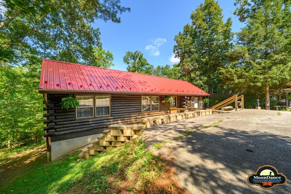 A log cabin with a red roof, wooden steps leading to the entrance, and a gravel driveway. - Hot tub, Pet Friendly, Woodsy home near Downtown (Nashville)