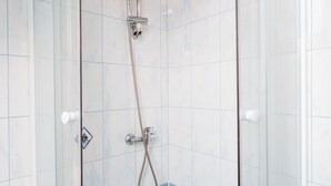 Ducha con cerramiento de vidrio, cabezal de ducha de mano y grifo empotrado.