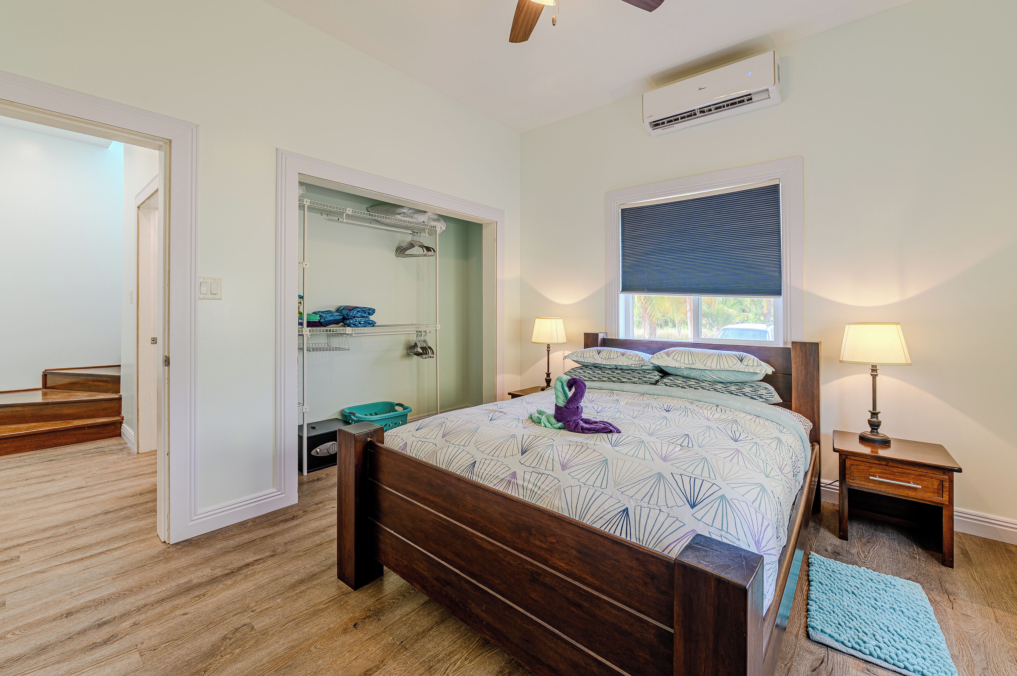 Un dormitorio con cama de madera, dos lámparas de noche, una ventana con persianas, un vestidor y un baño con ducha e inodoro.