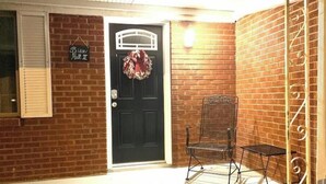 A brick exterior with a black door, a hanging wreath, and a metal chair.