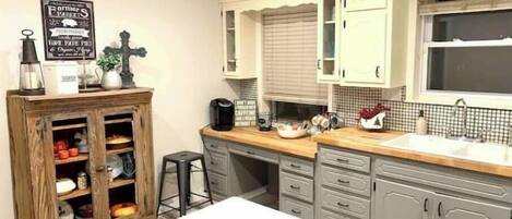 A kitchen with white cabinets, a wooden table, and a sign on the wall.