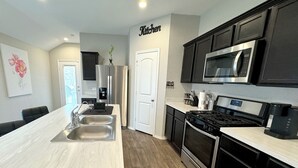A modern kitchen with a large island, stainless steel appliances, and dark cabinetry. - Modern 3br/2ba with 3 king beds · Pool · Pets OK! (Patton Village)