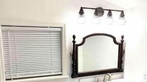 A bathroom with a white toilet, a white sink with a dark mirror above it, and a window with blinds.