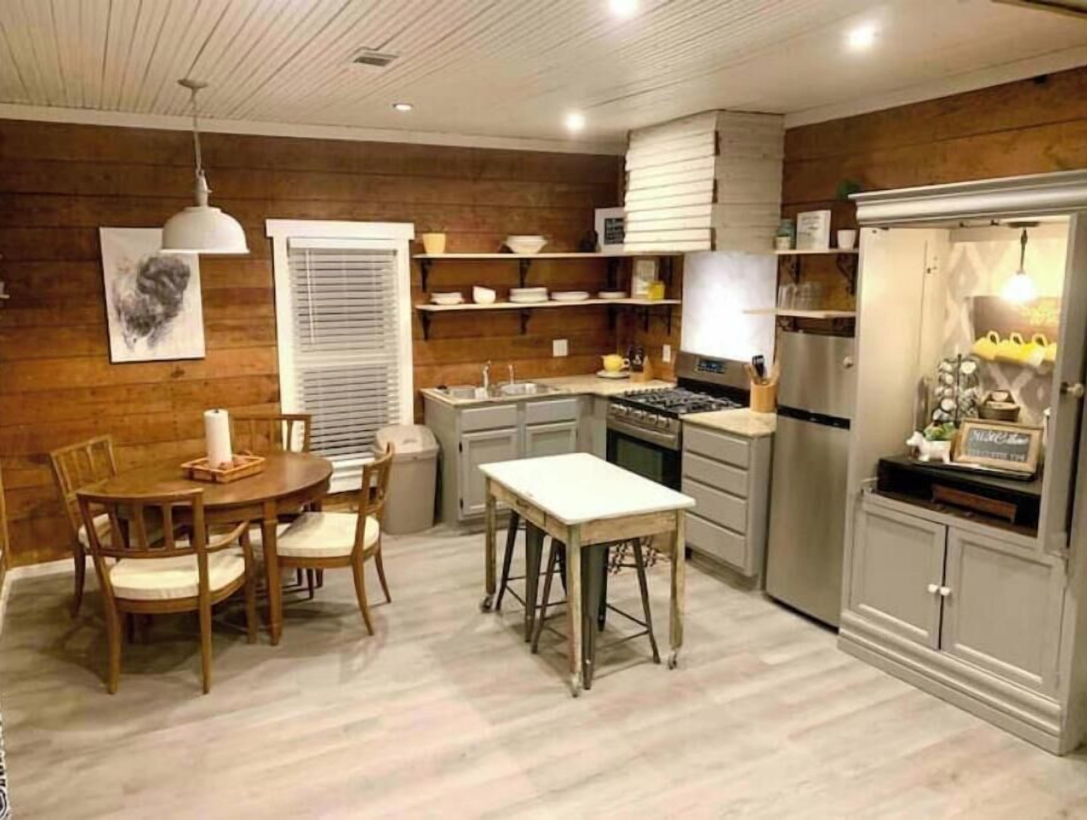 A compact kitchen with wooden walls, a dining area with a table and chairs, and a refrigerator.