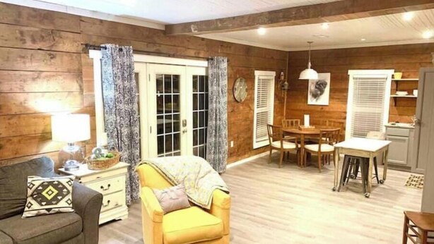A living room with a sofa, armchair, dining table, and kitchen area.