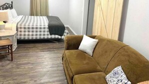 A bedroom with a bed, a brown sofa, a desk with a lamp, and a sliding wooden door.