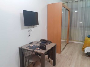 A small room with a desk, chair, and a television mounted on the wall.