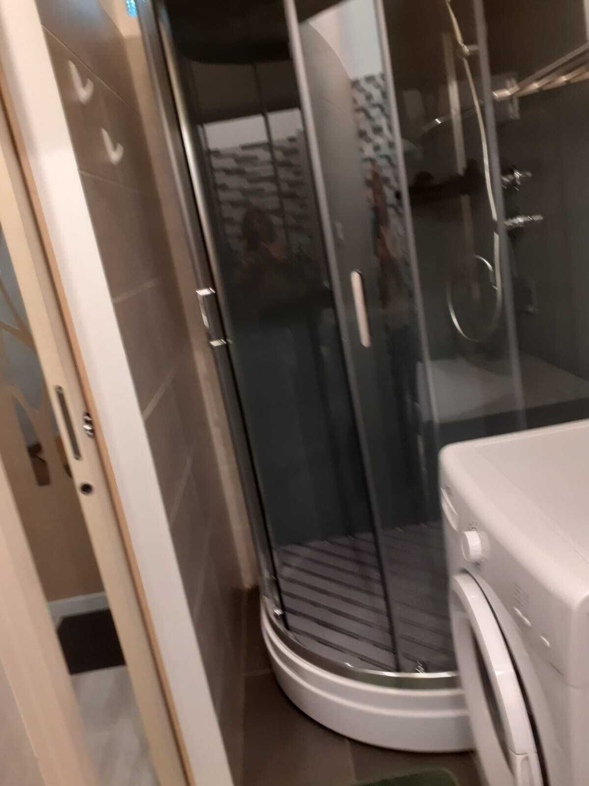 Un baño moderno con cabina de ducha de vidrio, lavadora integrada y suelo de baldosas.
