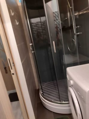 A modern bathroom with a glass shower enclosure, a built-in washing machine, and a tiled floor.