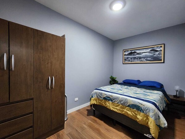 Un dormitorio con cama, armario, mesita de noche, lámpara y un cuadro en la pared.