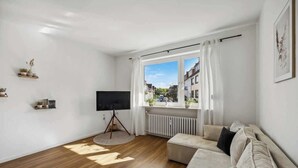 A modern living room with a large window, a flat-screen TV, and a sofa.
