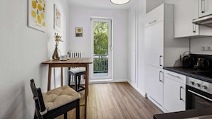 A compact kitchen with white cabinets, a dining table with chairs, a pendant light, and a view through a glass door to an outdoor area.
