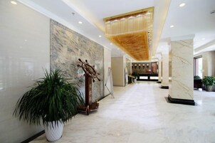 Un vestíbulo de hotel con piso de mármol, una planta grande en maceta, una escultura de madera decorativa y un candelabro.